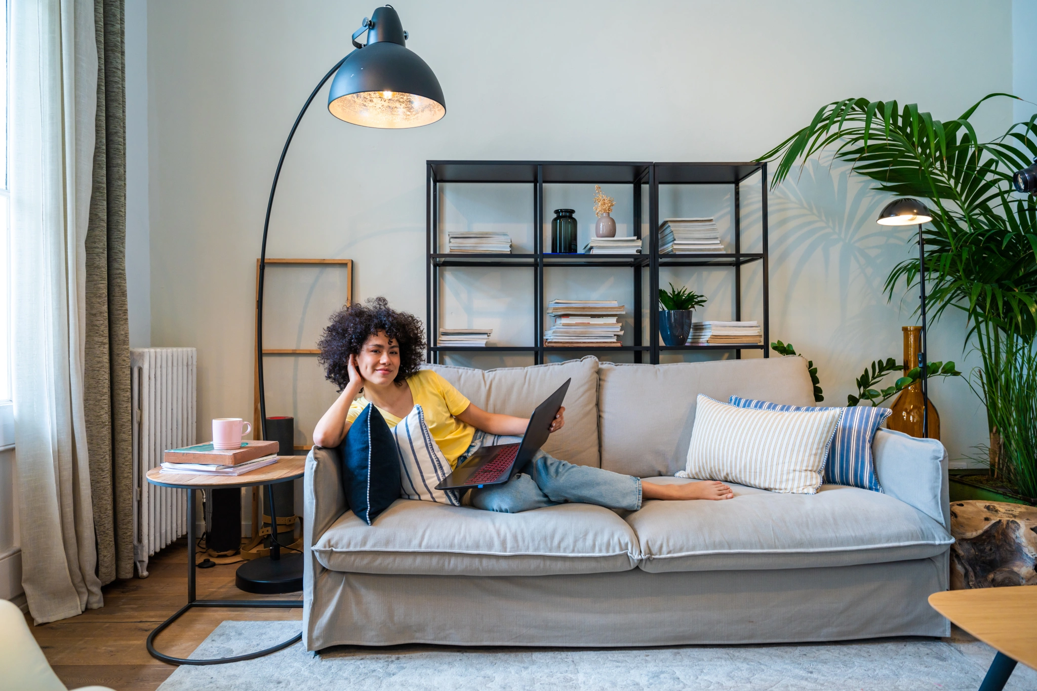 Woman relaxing on a couch reading a book under a lamp.