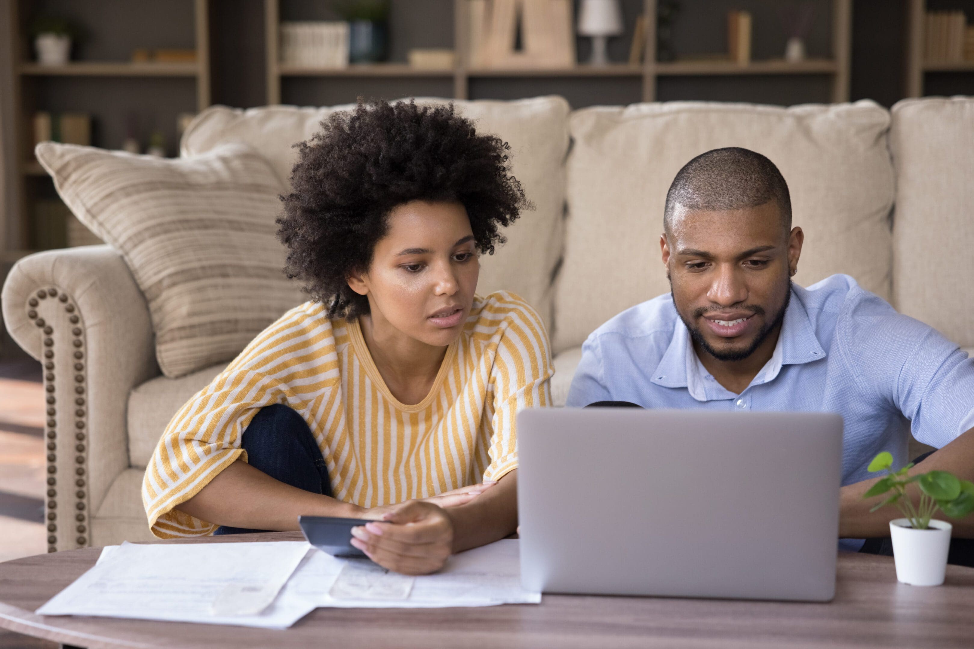 A couple reviewing documents while using a laptop on a couch.