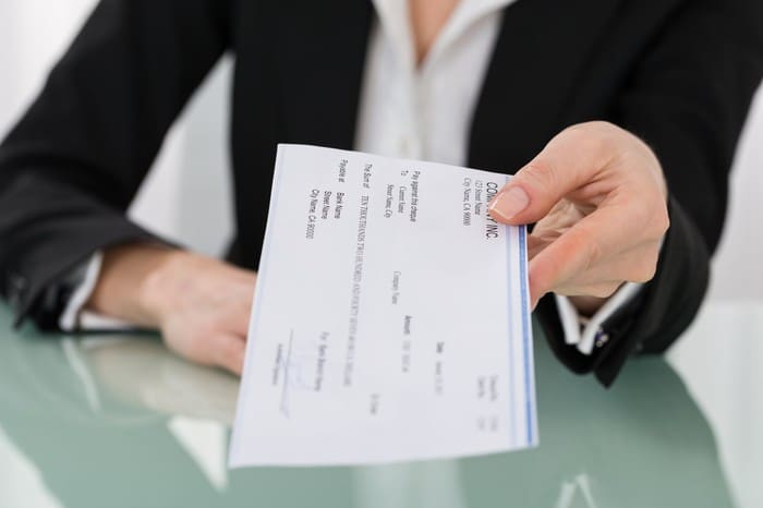 A person hands over a check to another individual across a desk.