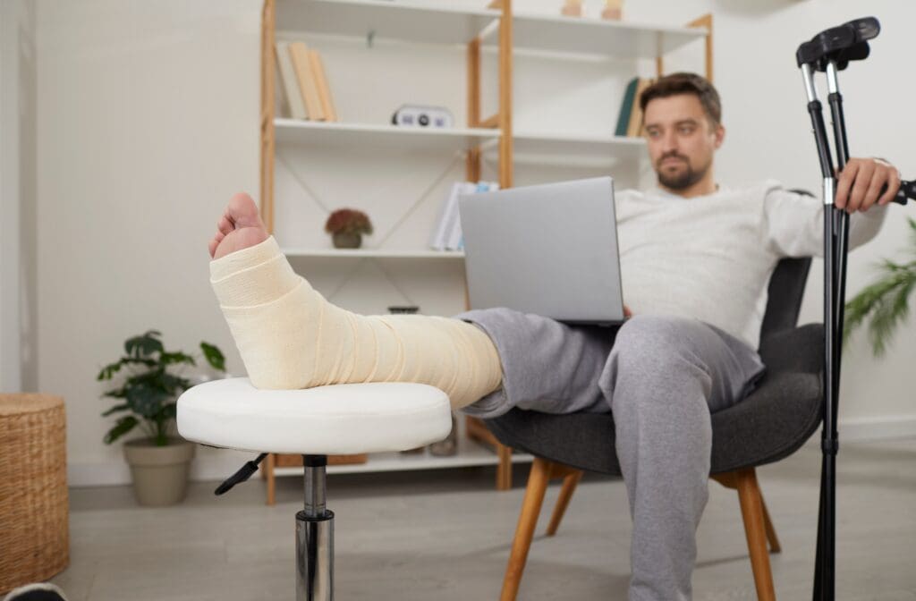 Man with leg cast working on laptop at home.