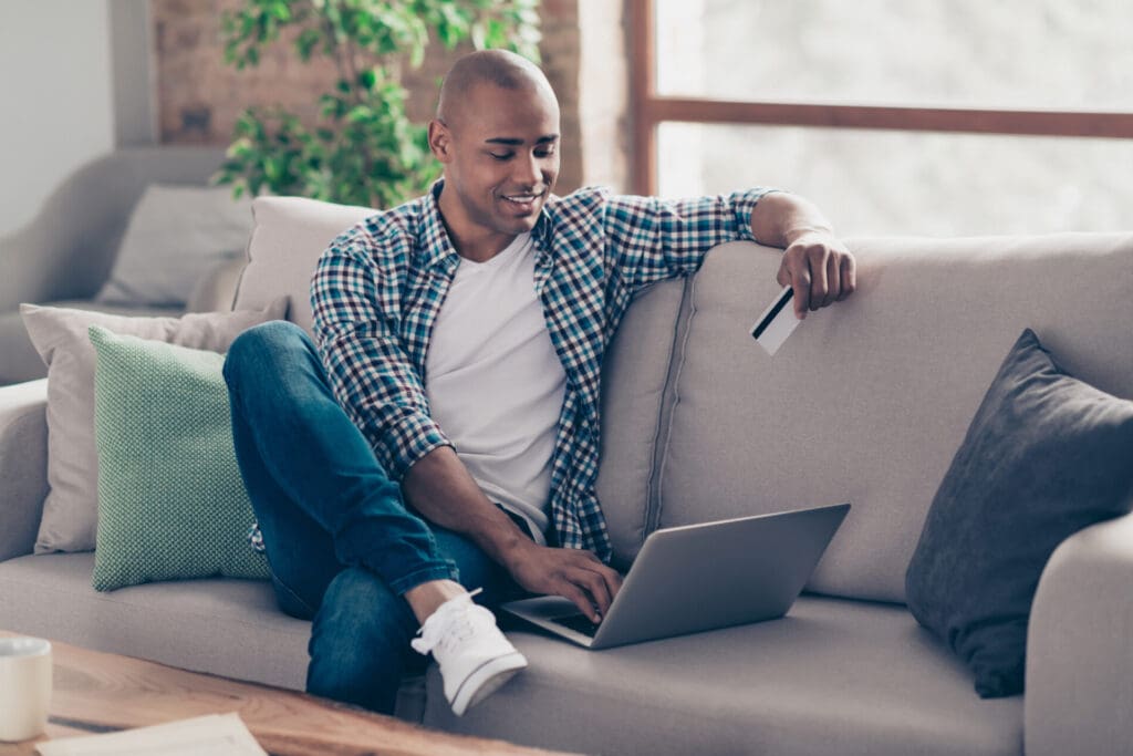 Man relaxing on couch using smartphone and laptop.