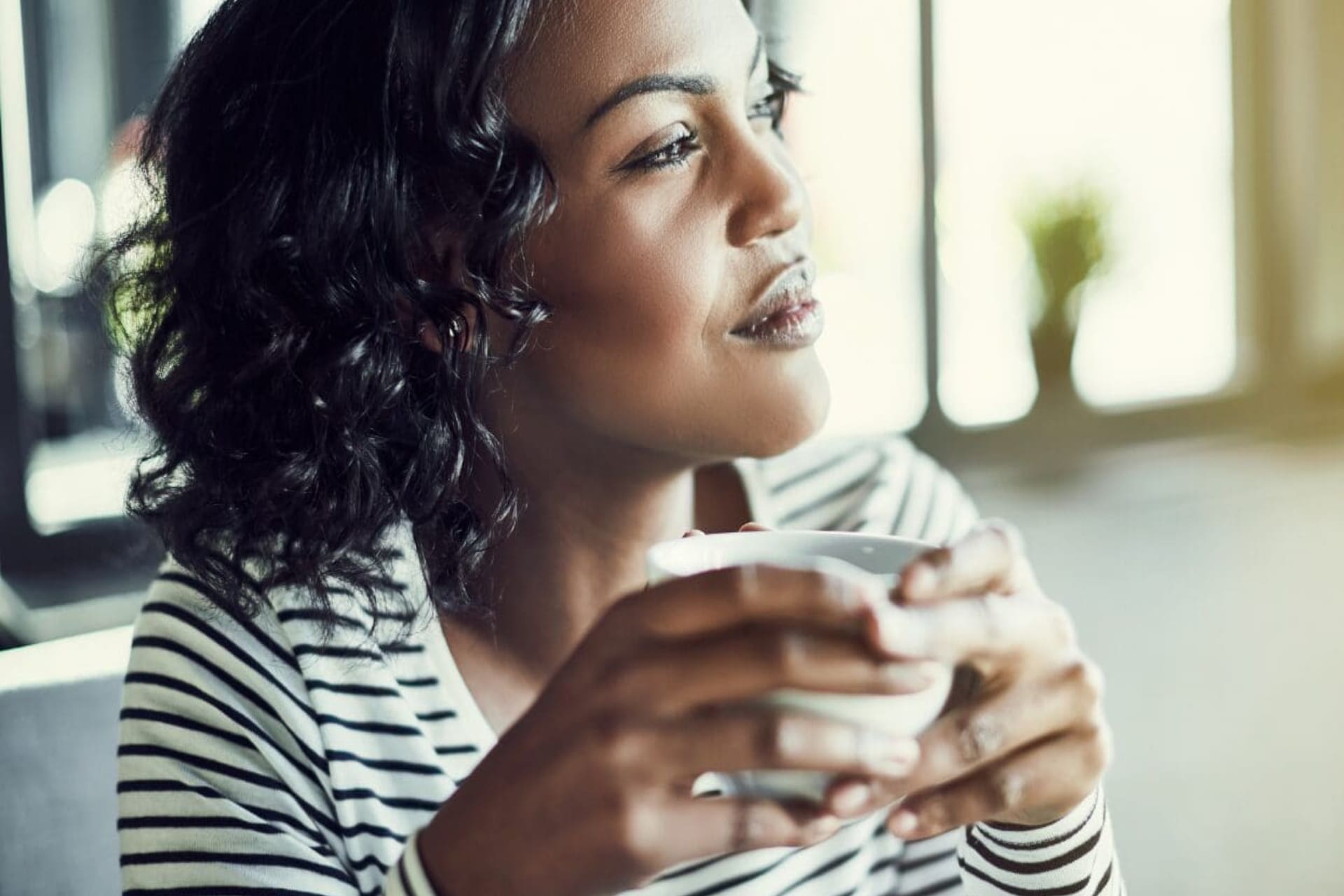 Woman enjoying a warm beverage and looking thoughtfully outside.