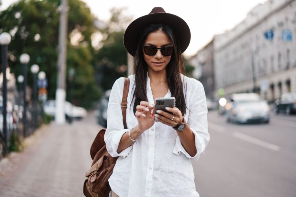 Woman in white shirt and hat using smartphone outdoors.
