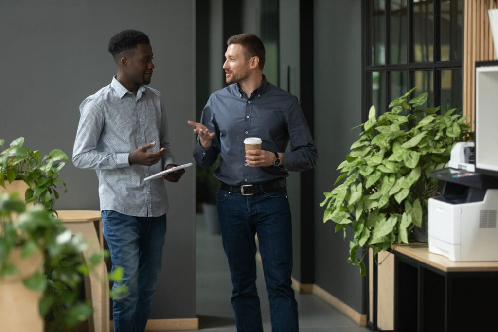 Two colleagues discussing work while walking in an office corridor.