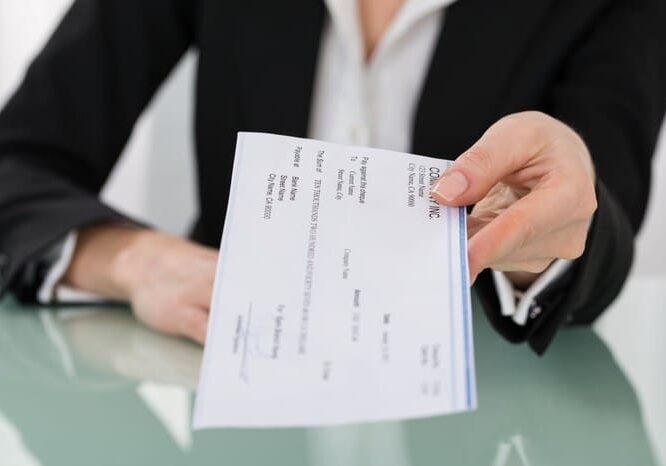 A person hands over a check to another individual across a desk.
