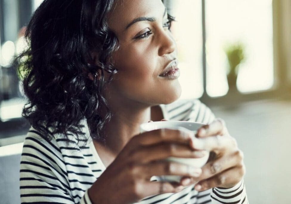 Woman enjoying a warm beverage and looking thoughtfully outside.