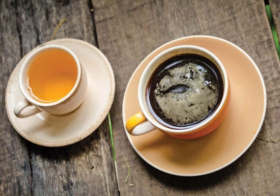 A cup of black coffee and a cup of tea on a wooden table.